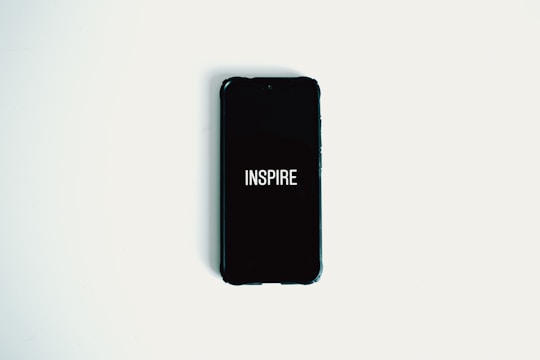 A smartphone with a black screen displaying the word 'INSPIRE' in white text is lying on a plain white surface.
