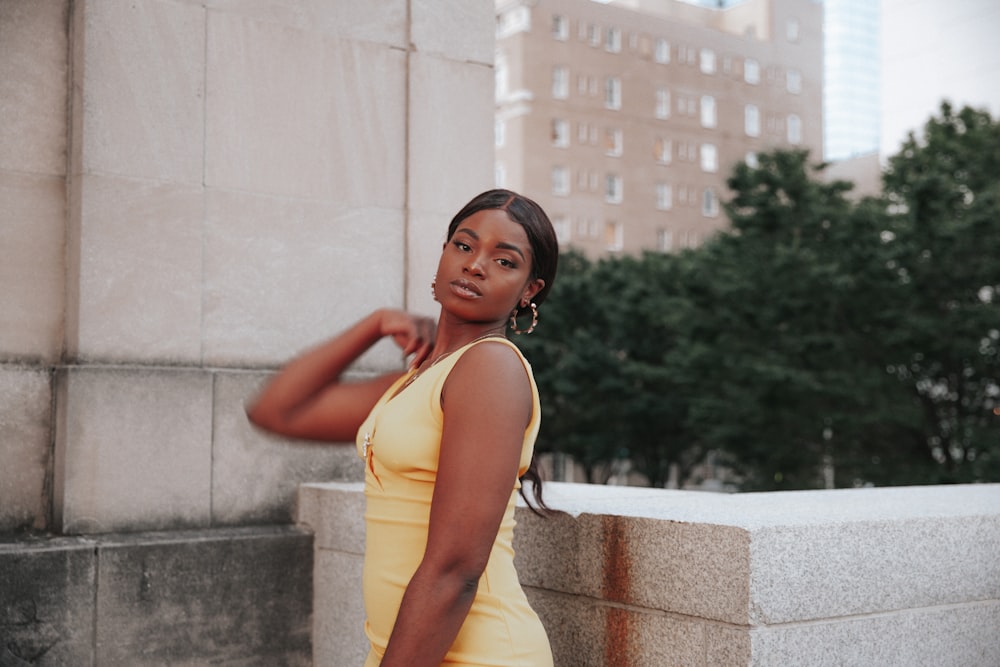 woman in yellow tank dress standing beside white concrete wall during daytime