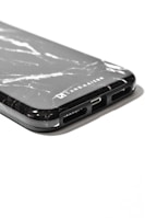 A close-up view of a smartphone case with a black marble pattern and the logo 'LARS KAIZER' engraved on it. The bottom part of the case shows cutouts for speakers and charging port.