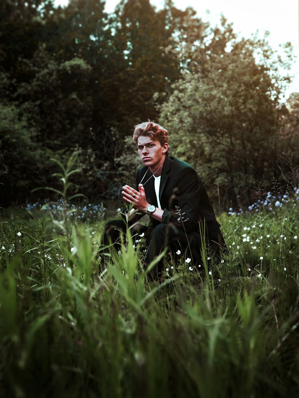 man in black suit jacket sitting on green grass field during daytime