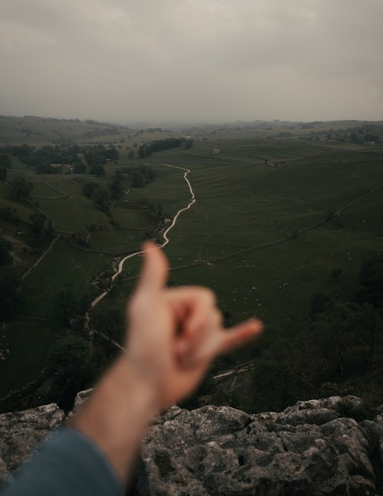 person pointing on green grass field during daytime in Malham Cove United Kingdom