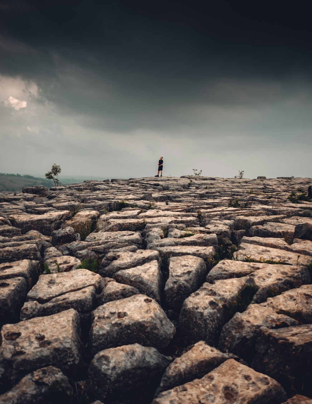 person standing on rocky hill under gray sky