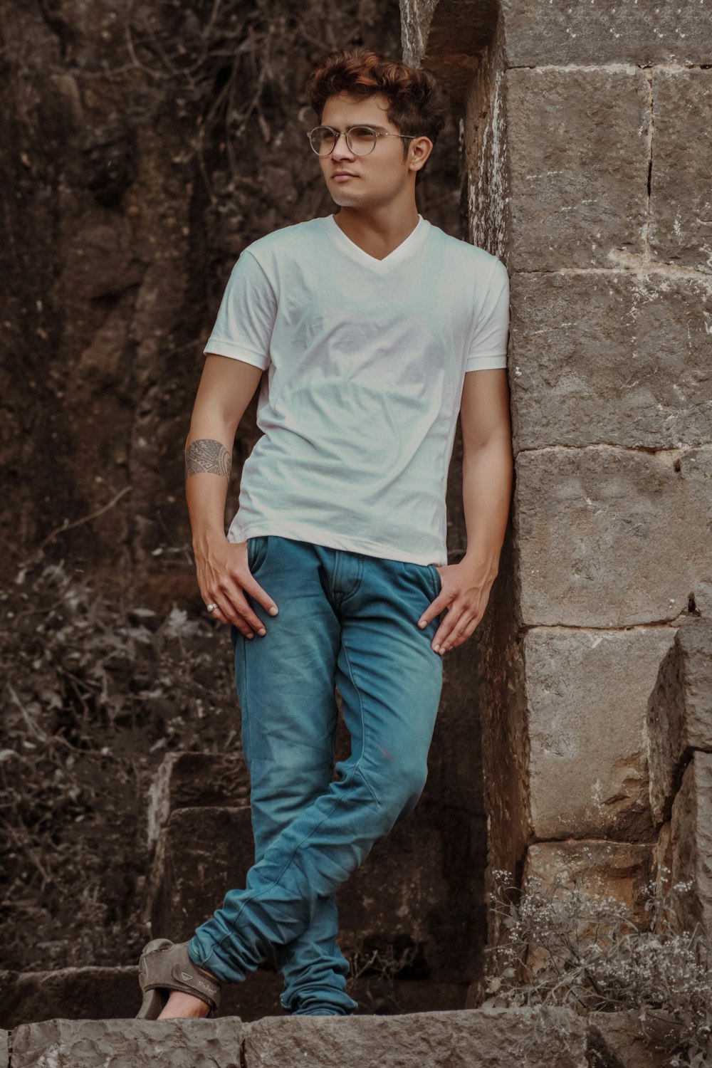man in white crew neck t-shirt and blue denim jeans leaning on brown concrete wall