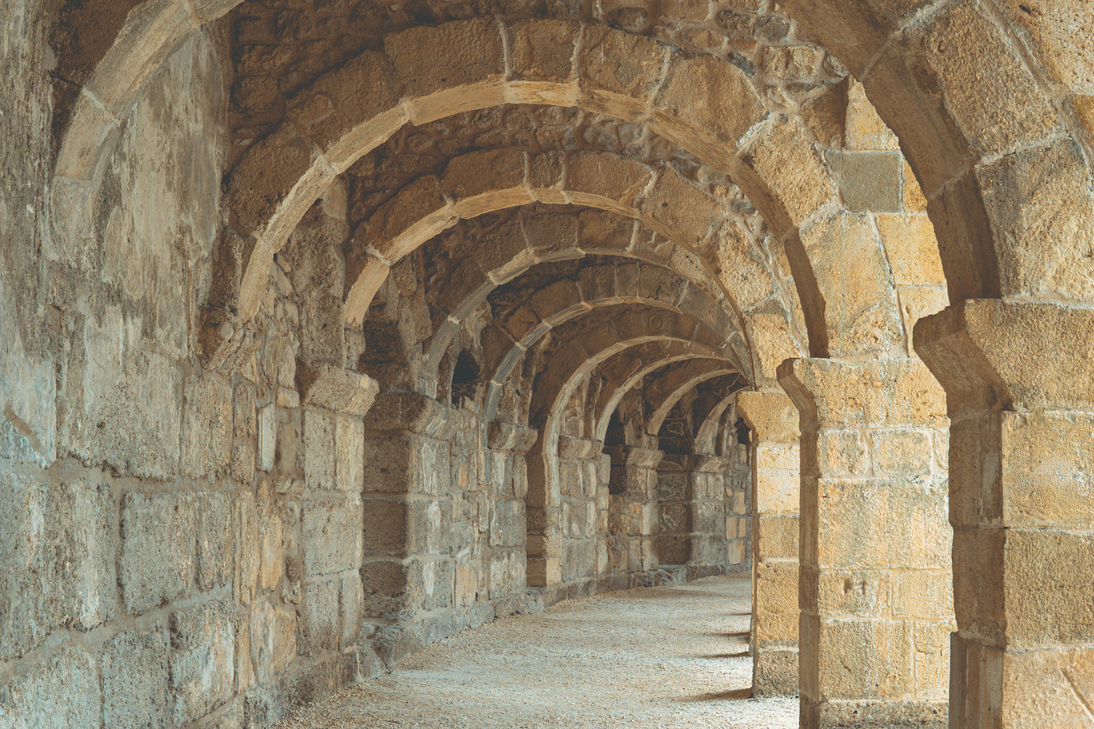 A vaulted stone arcade corridor inside the ancient Aspendos theatre, arches receding into warm light.