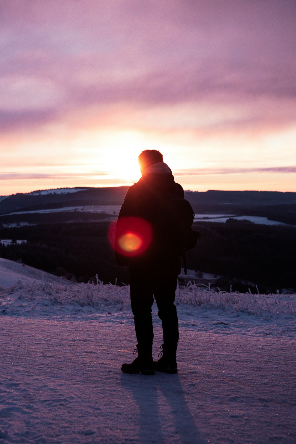 homme en veste noire debout sur le sol enneigé pendant le coucher du soleil