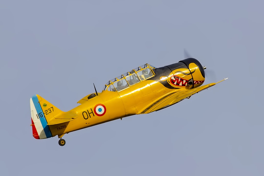 yellow and blue jet plane in mid air, T-6 climbing