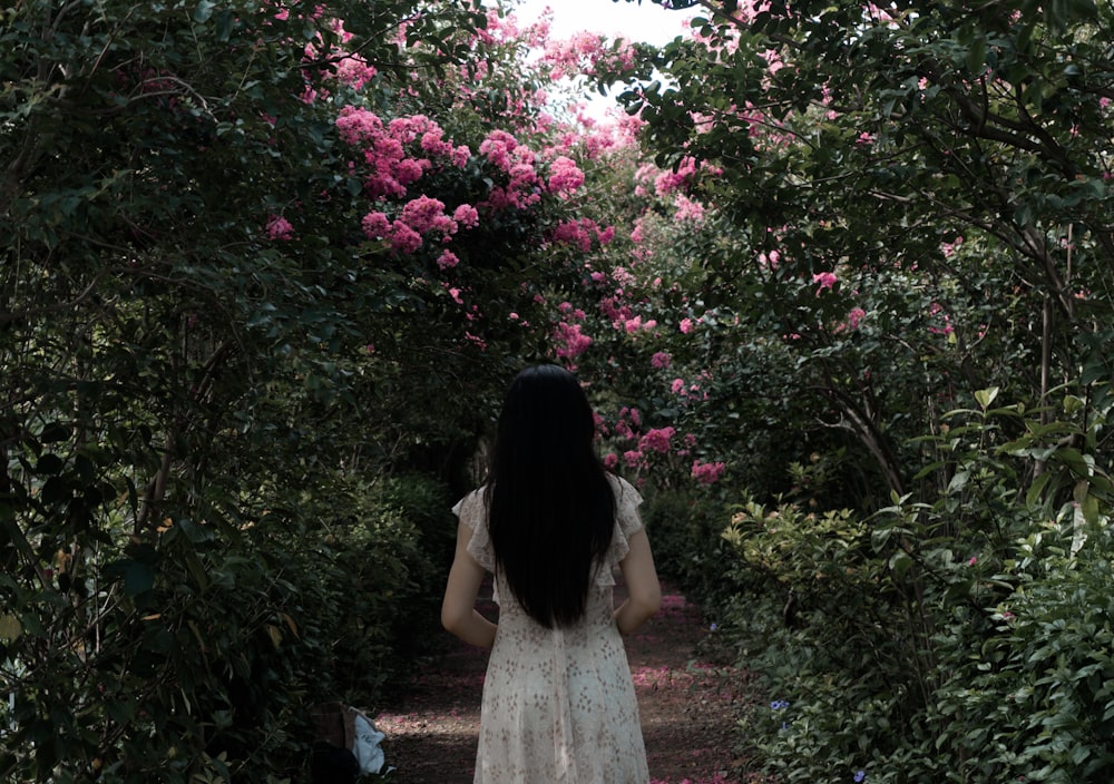 woman in white dress standing near pink flowers