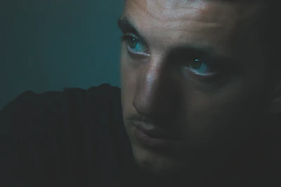 Close-up of the main character's intense gaze, shadows casting across his face in a dimly lit prison corridor.