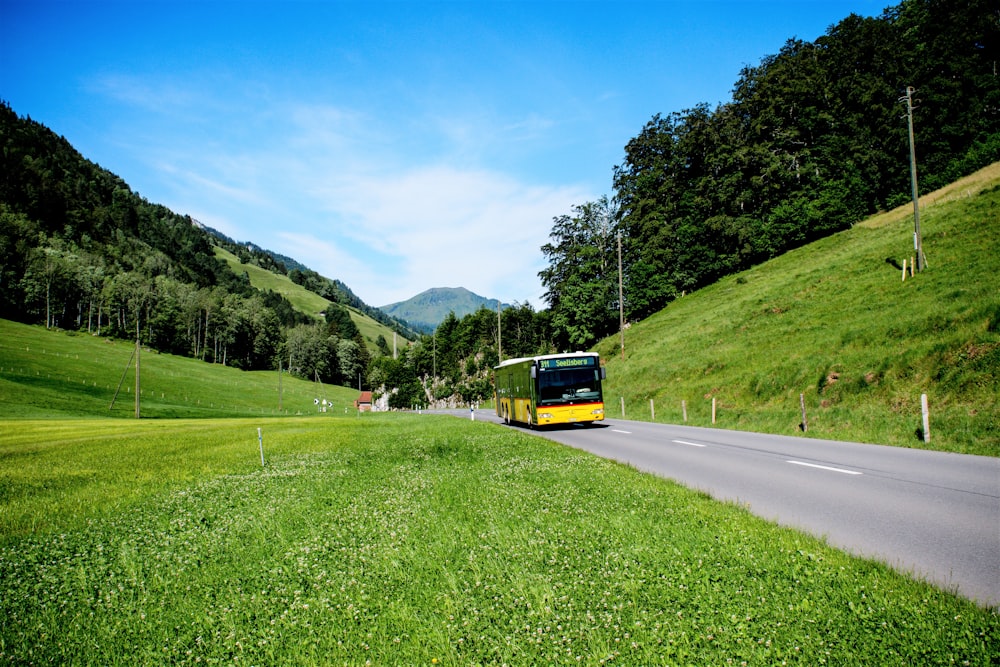 yellow and black bus on road near green grass field and green mountains during daytime