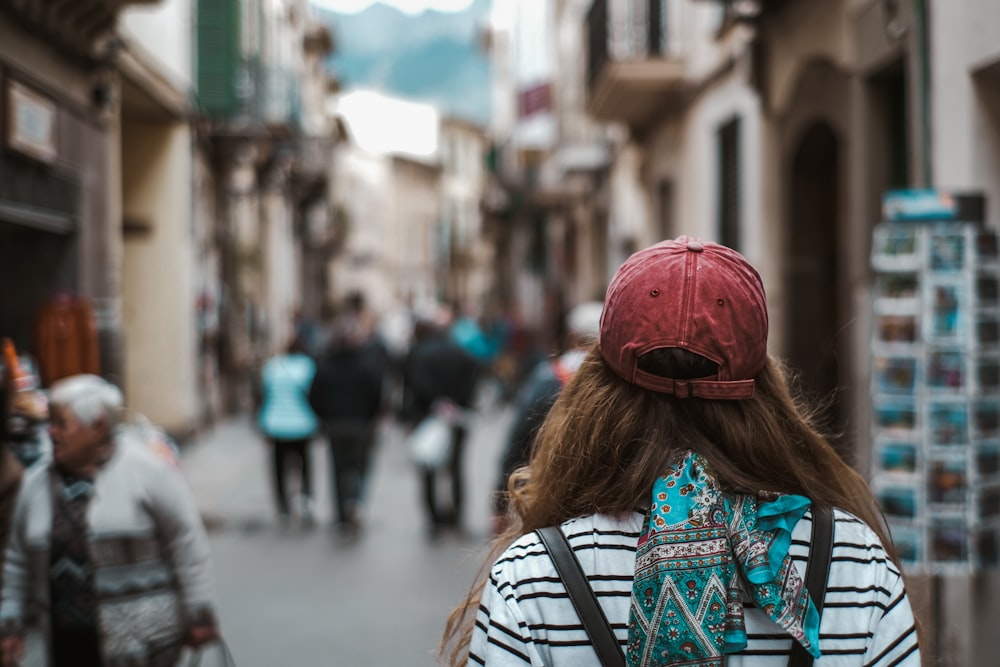 donna in berretto a maglia rosso e camicia con stampa tribale blu e bianca che cammina per strada durante