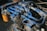A complex network of blue hydraulic tubes connected to a metal machinery component, with a visible orange filter bearing text in the background. The surface exhibits signs of wear and dirt, indicating usage and exposure to industrial conditions.
