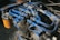 A complex network of blue hydraulic tubes connected to a metal machinery component, with a visible orange filter bearing text in the background. The surface exhibits signs of wear and dirt, indicating usage and exposure to industrial conditions.