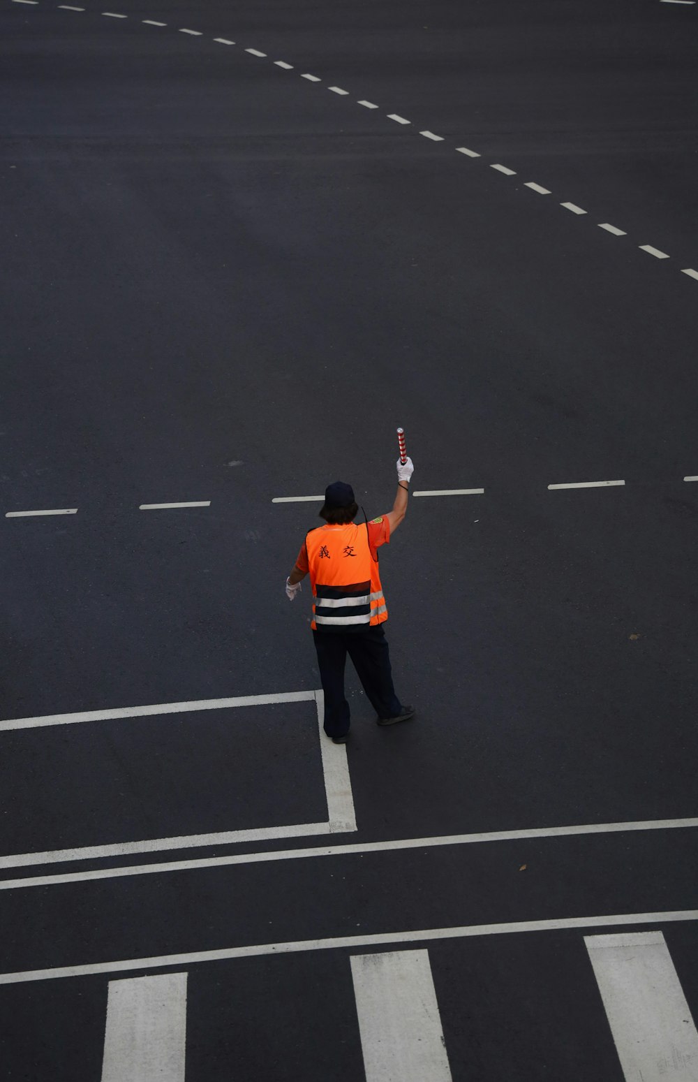 man in orange jacket and black pants standing on black asphalt road