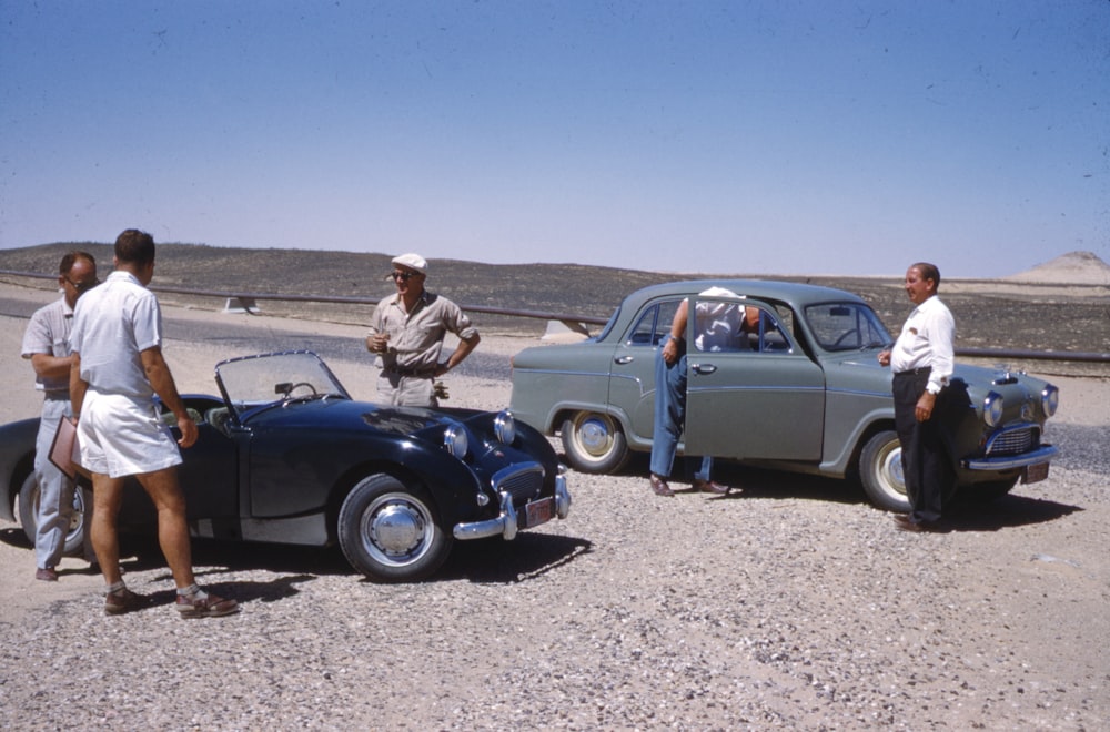 man in brown jacket standing beside blue volkswagen beetle