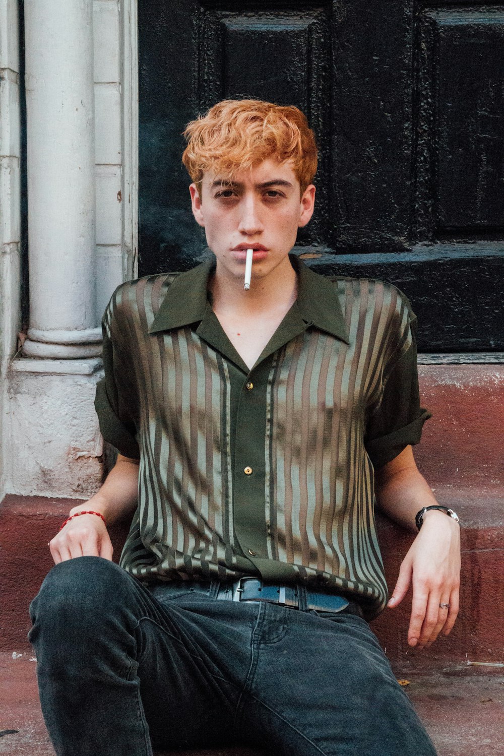 man in green and black striped button up shirt and blue denim jeans sitting on gray