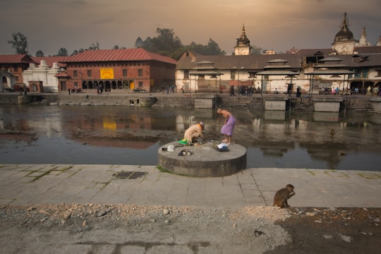 woman in blue long sleeve shirt sitting on gray concrete bench near body of water during in Pashupatinath Nepal