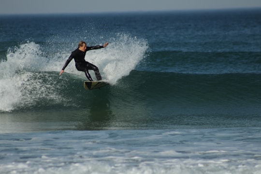 man in black and red wet suit surfing on sea during daytime in Port Alfred South Africa