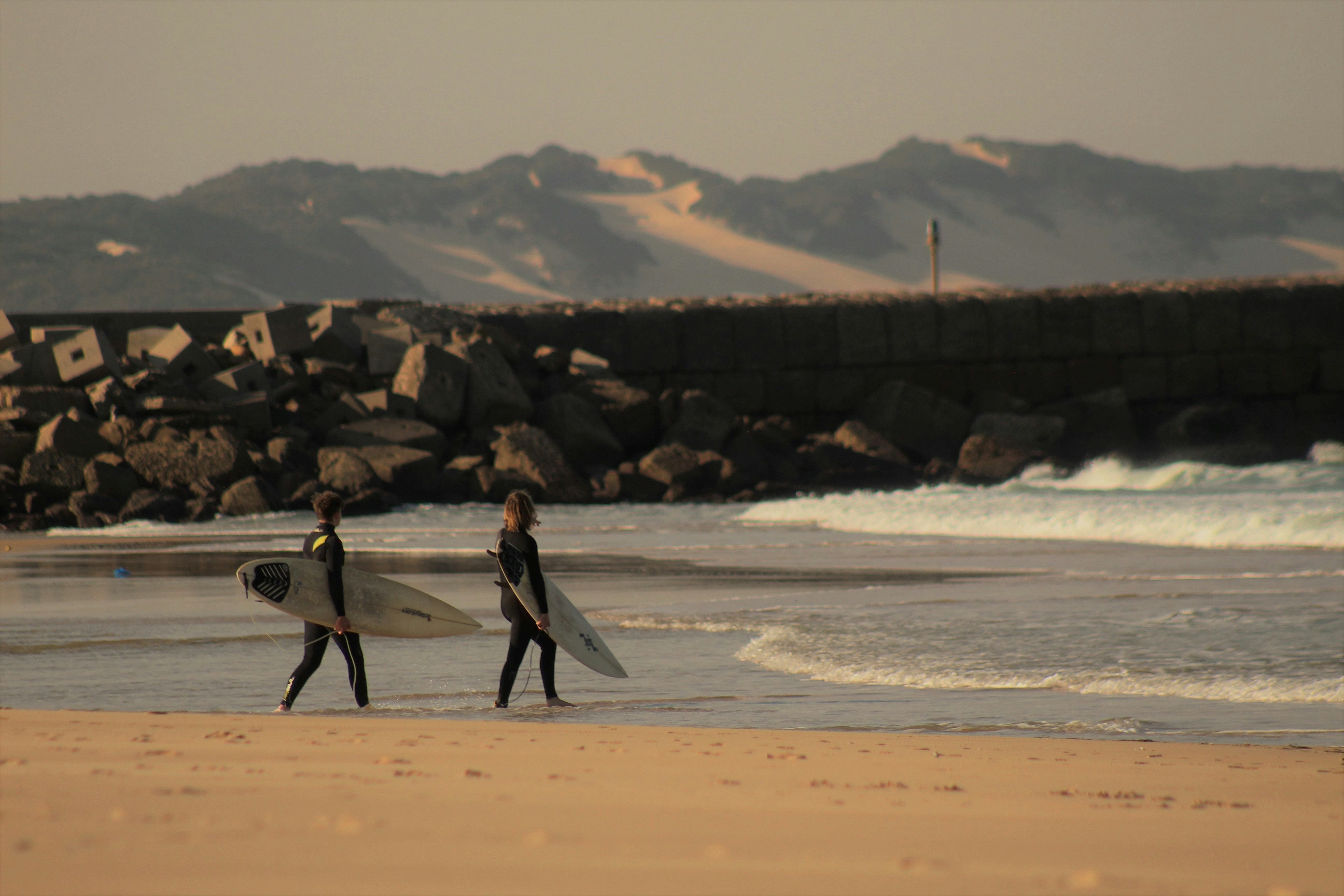 man and woman holding white surfboard walking on beach during daytime