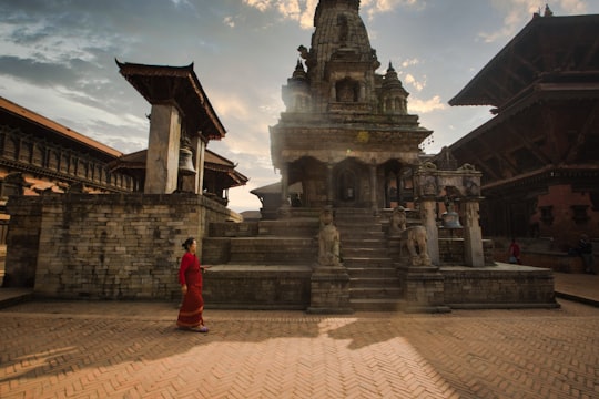 woman in red dress standing near temple during daytime in Durbar Square Nepal