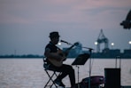 man in black shirt playing guitar near body of water during daytime