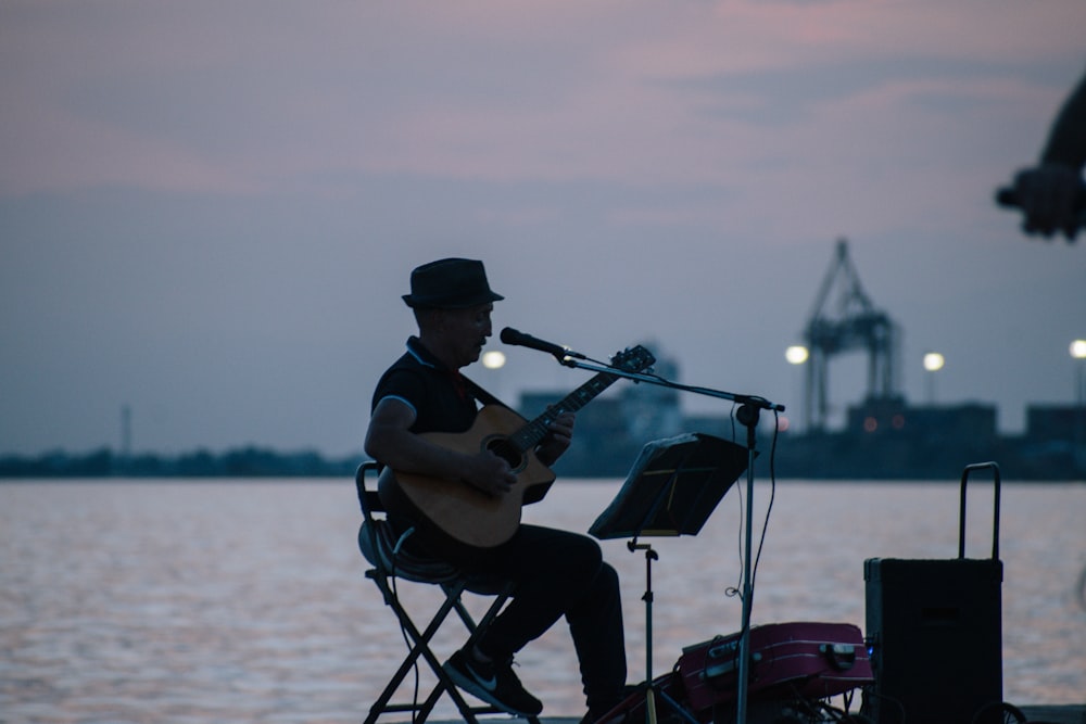 man in black shirt playing guitar near body of water during daytime