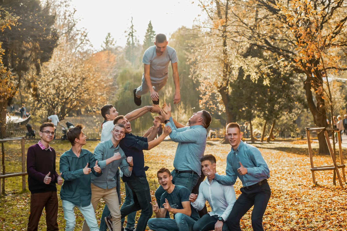 Groupe de jeunes adultes dans un parc en automne, l'un d'eux soulevé dans les airs par ses camarades