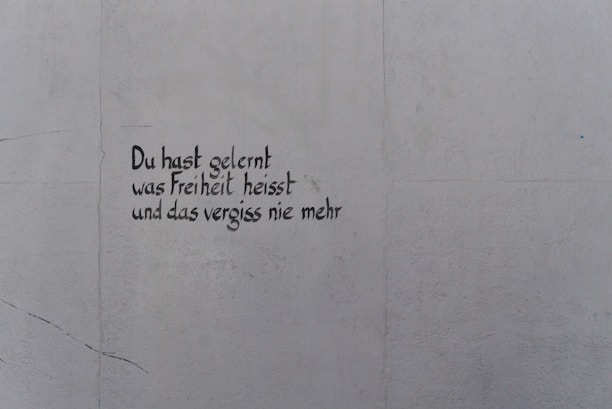 A light gray wall features text written in black, stylized handwriting. The words are in German and read, 'Du hast gelernt was Freiheit heisst und das vergiss nie mehr.'