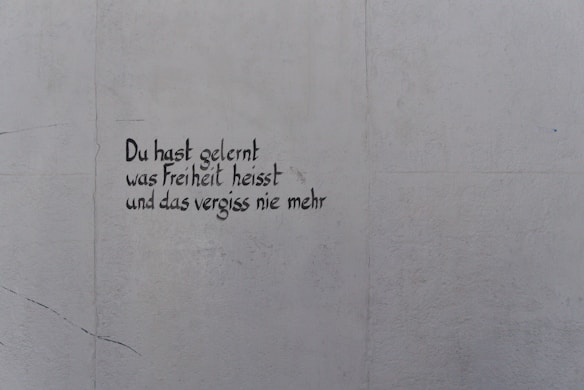 A light gray wall features text written in black, stylized handwriting. The words are in German and read, 'Du hast gelernt was Freiheit heisst und das vergiss nie mehr.'