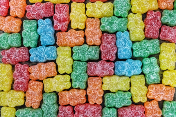A colorful assortment of gummy bear candies arranged closely together in a uniform pattern. The candies are covered in a light dusting of sugar.