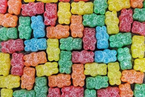 A colorful assortment of gummy bear candies arranged closely together in a uniform pattern. The candies are covered in a light dusting of sugar.