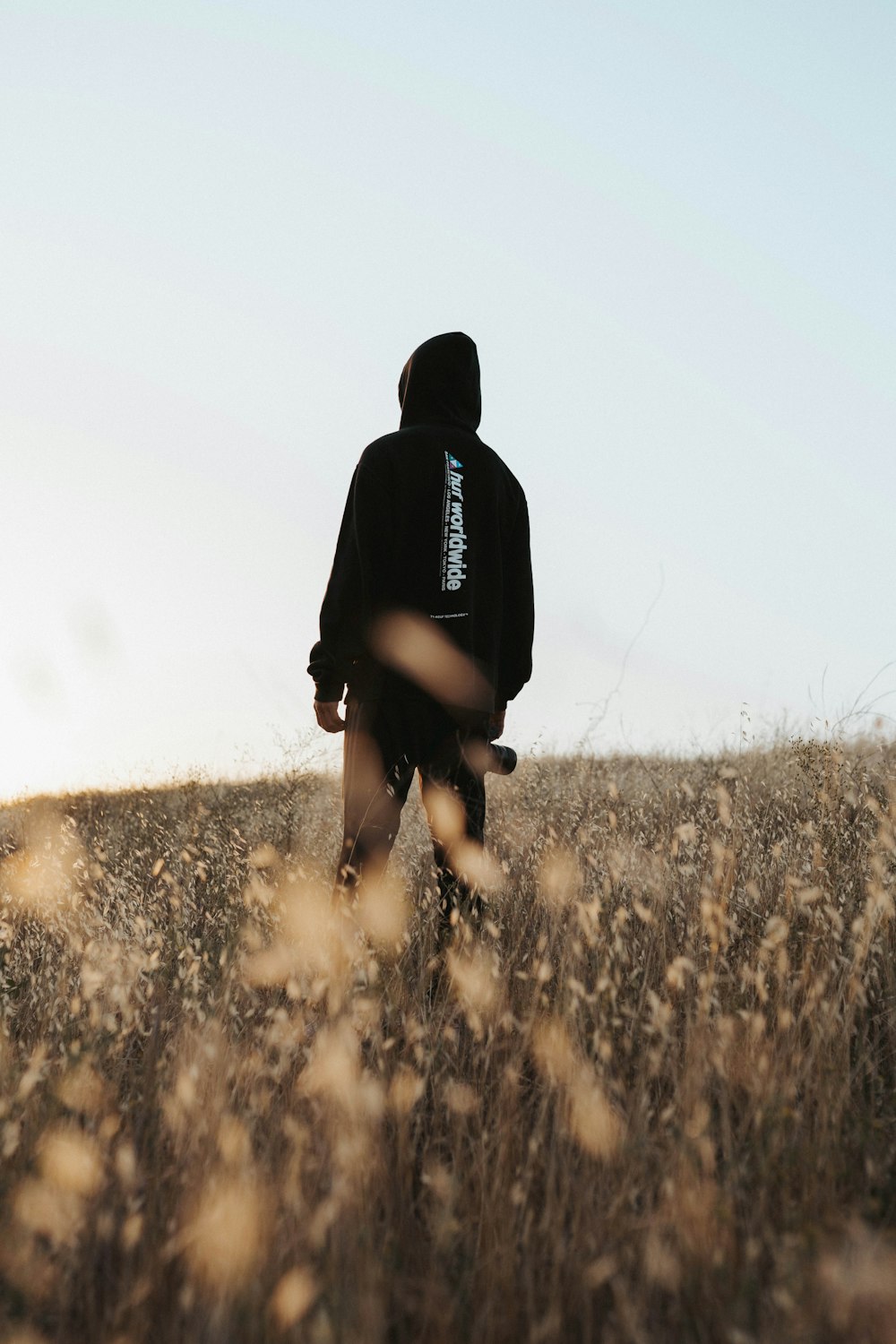person in black hoodie walking on brown grass field during daytime