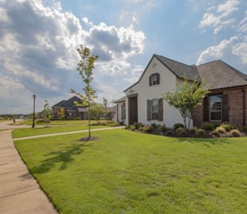 white and brown house near green grass field under white clouds and blue sky during daytime