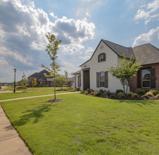 white and brown house near green grass field under white clouds and blue sky during daytime