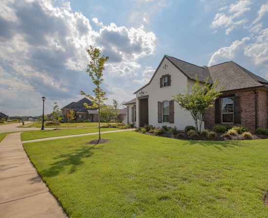 white and brown house near green grass field under white clouds and blue sky during daytime