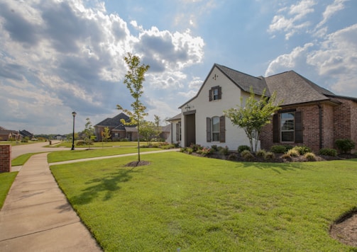 white and brown house near green grass field under white clouds and blue sky during daytime