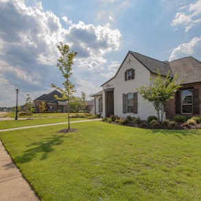 white and brown house near green grass field under white clouds and blue sky during daytime