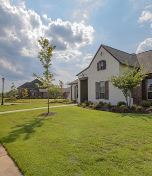 white and brown house near green grass field under white clouds and blue sky during daytime