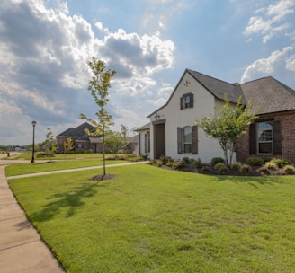 white and brown house near green grass field under white clouds and blue sky during daytime