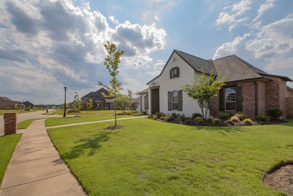 white and brown house near green grass field under white clouds and blue sky during daytime