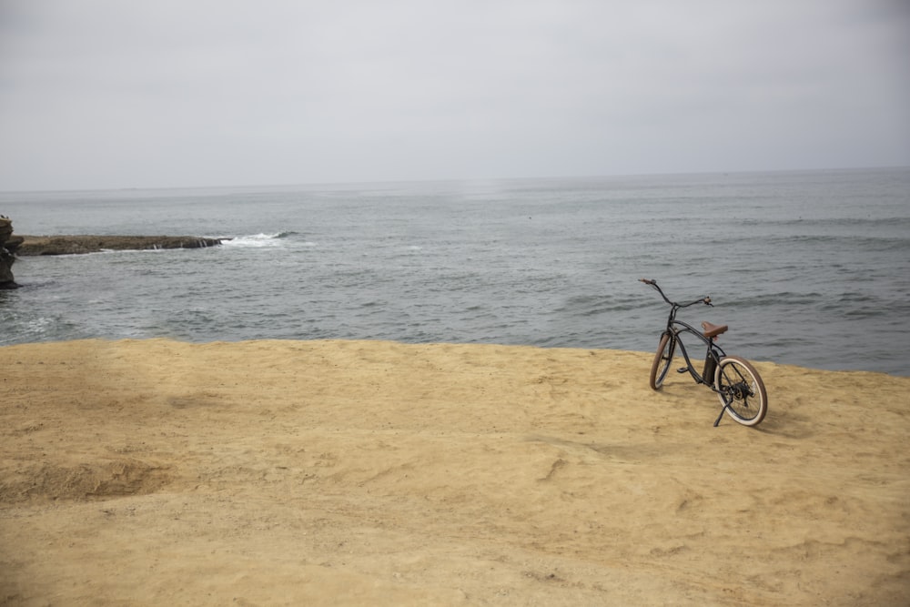 black bicycle on brown sand near body of water during daytime