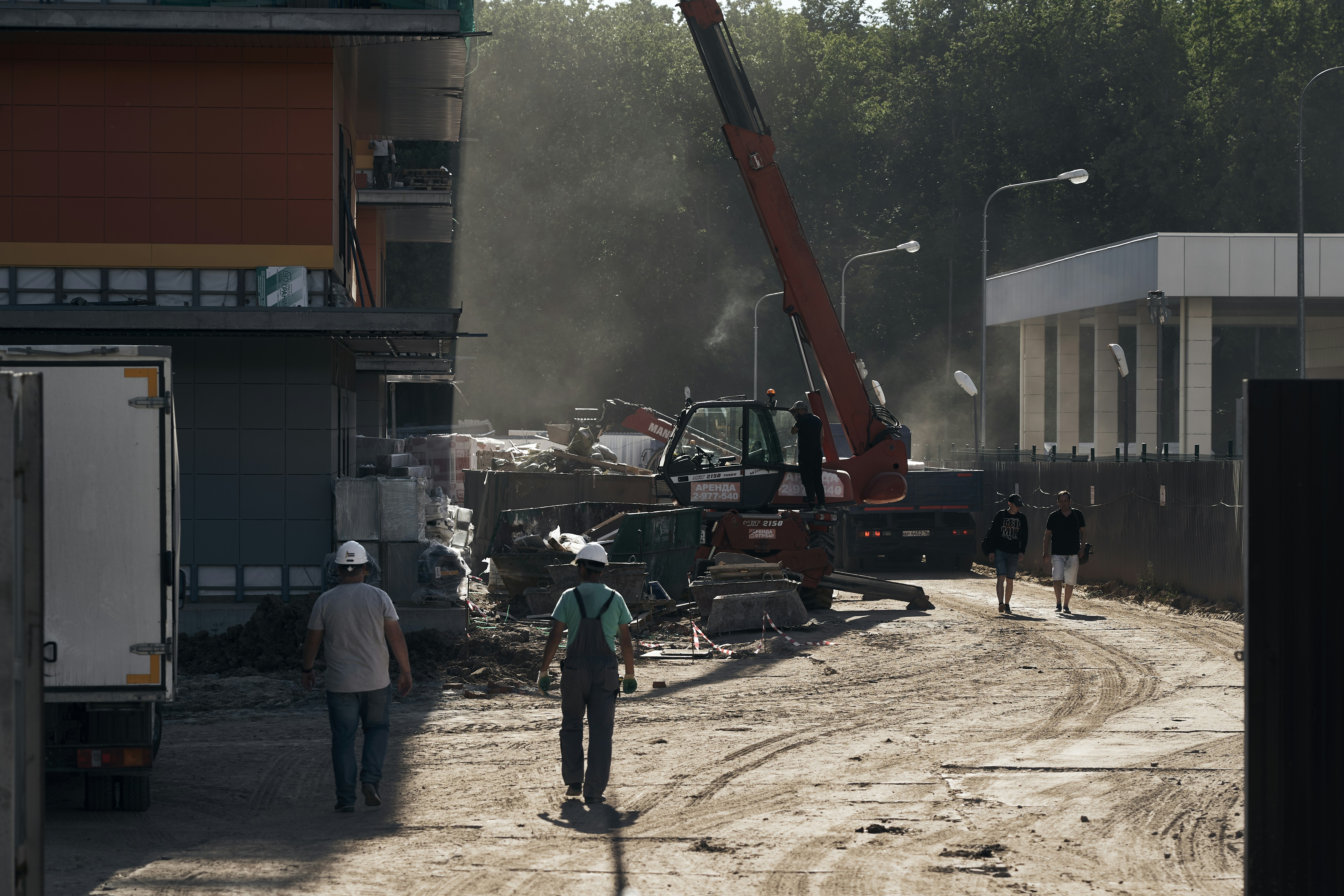 Bygningsarbejdere og lastbiler på en støvet byggeplads udendørs.