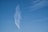 A wisp of white cloud stretches vertically against a bright blue sky, forming a feather-like shape. Thin, wispy clouds are scattered to the right, creating a serene backdrop.