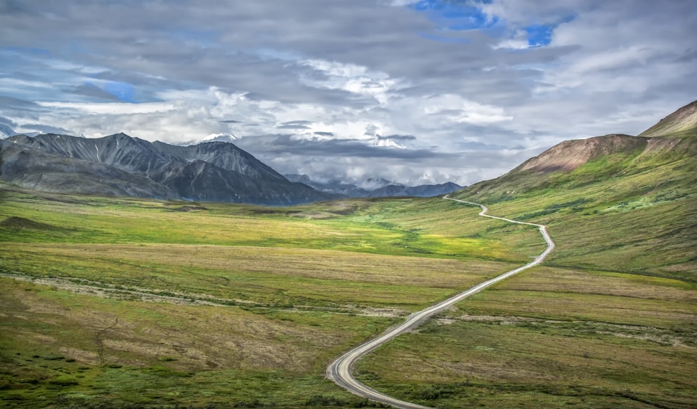 green grass field near mountain under cloudy sky during daytime