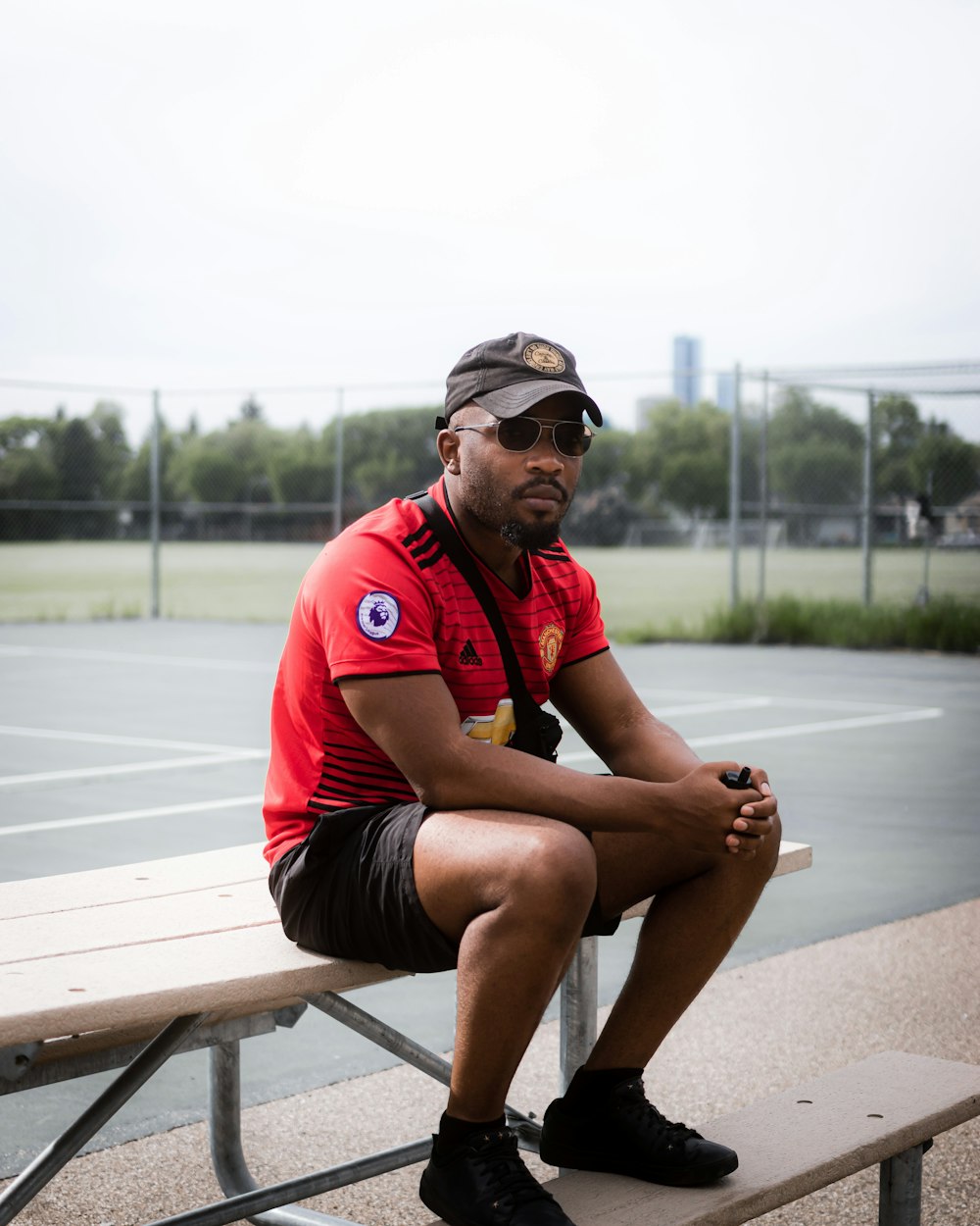 man in red polo shirt sitting on brown wooden bench during daytime