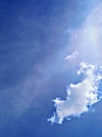 A large fluffy cloud is floating in a bright blue sky. The cloud has a soft, white texture with slightly irregular edges, set against a clear backdrop.