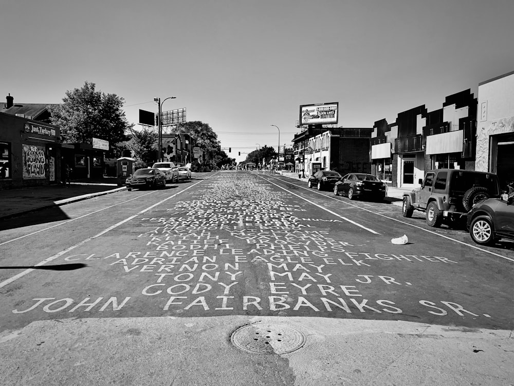 grayscale photo of city street with cars parked on side