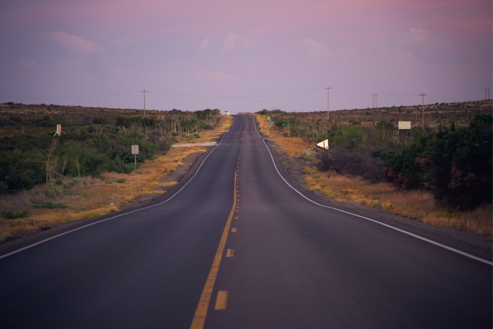 black asphalt road between green grass field under blue sky during daytime