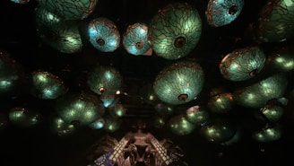 Multiple green, ornate, glass lamps with intricate patterns are suspended from the ceiling. They create a mesmerizing visual effect with warm light shining through stained glass, casting a soft glow in a dimly lit environment.