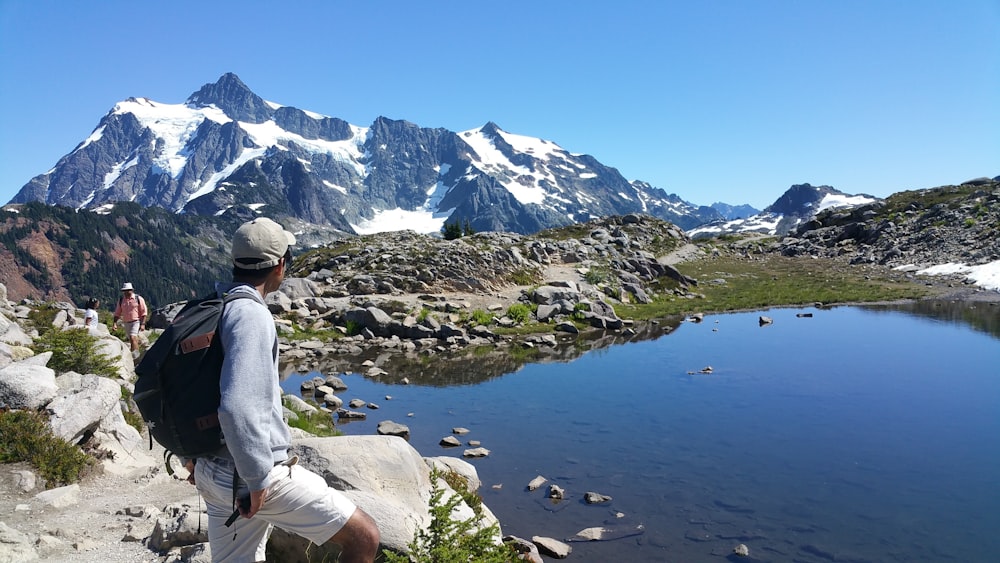 man in gray hoodie sitting on rock near lake during daytime