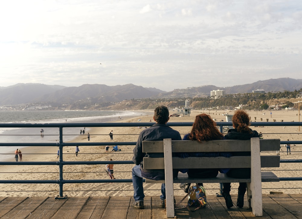 2 women sitting on bench looking at the sea during daytime